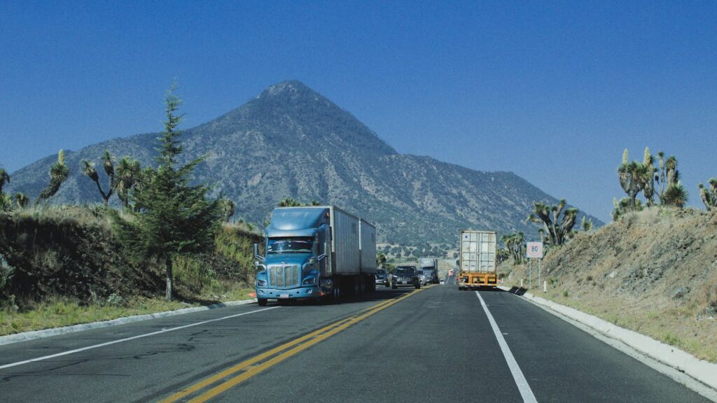 Trucks driving on a highway with a mountain backdrop under a clear blue sky.