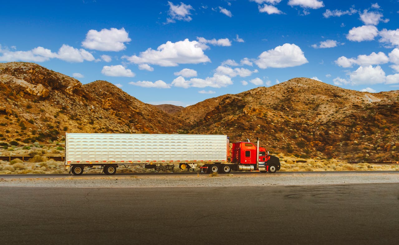 A vibrant red semi-truck travels through a desert highway with mountain views in Nevada.